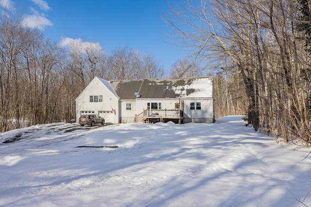 snow covered rear of property featuring a wooden deck and a garage