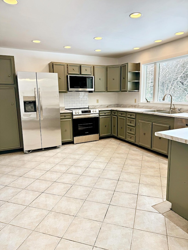 kitchen featuring a sink, green cabinets, light countertops, backsplash, and appliances with stainless steel finishes