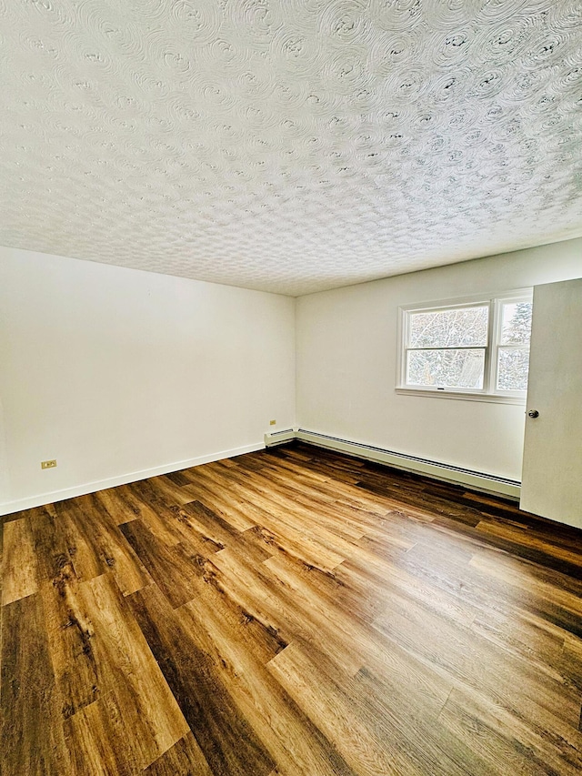 empty room featuring baseboard heating, baseboards, wood finished floors, and a textured ceiling