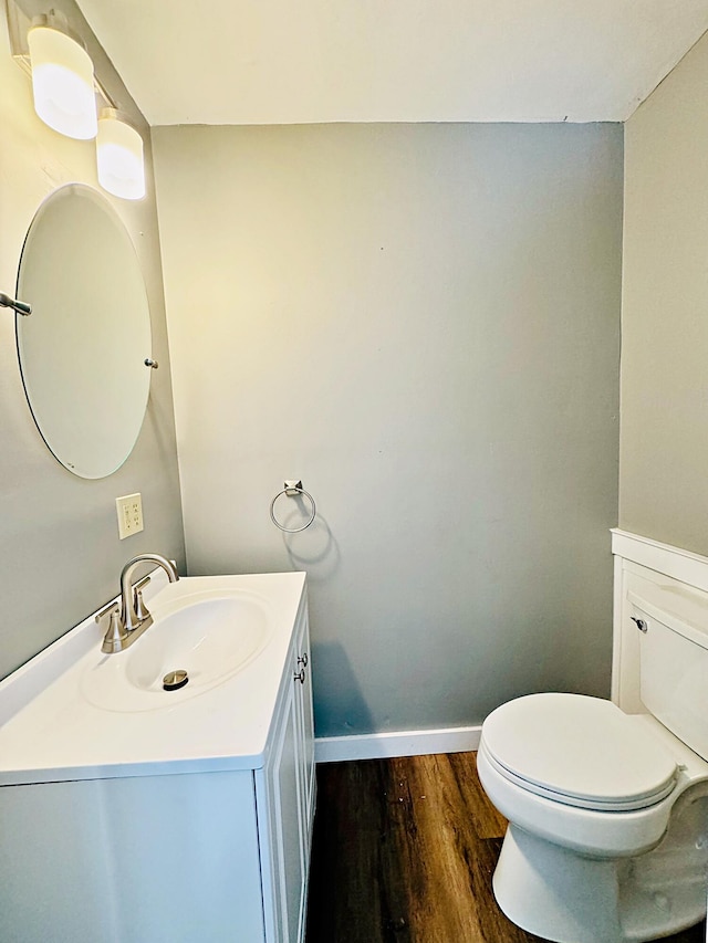 bathroom with toilet, vanity, wood finished floors, and baseboards