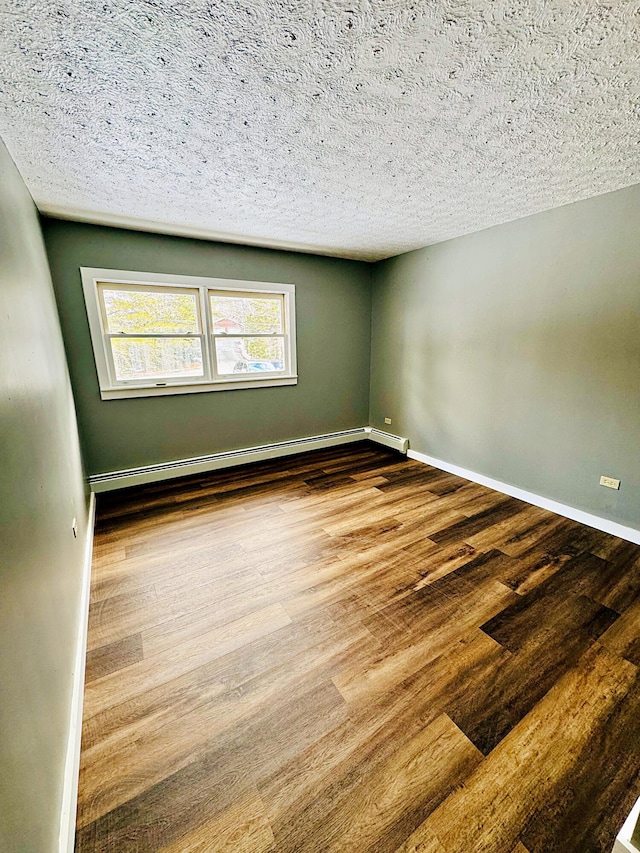 empty room with a baseboard radiator, baseboards, wood finished floors, and a textured ceiling