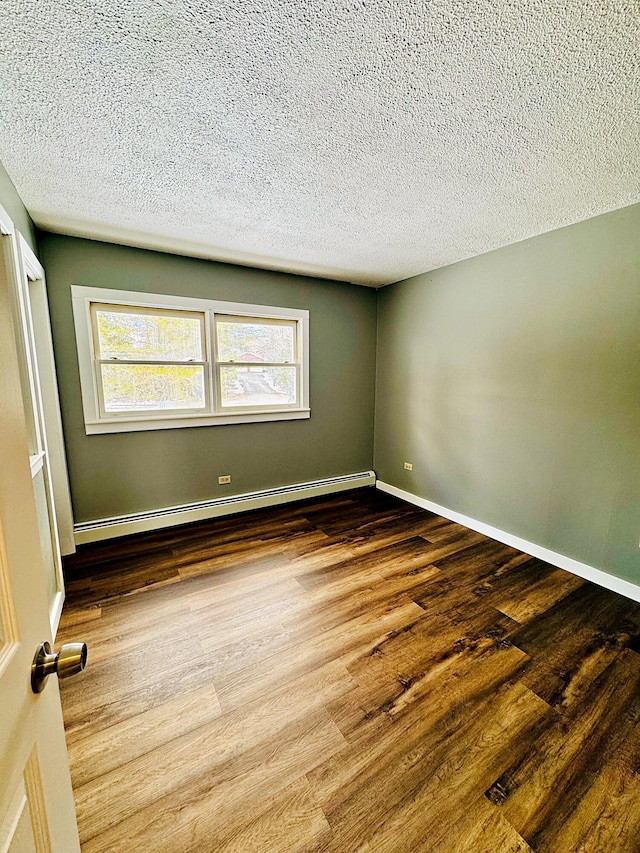 spare room featuring a baseboard heating unit, baseboards, wood finished floors, and a textured ceiling