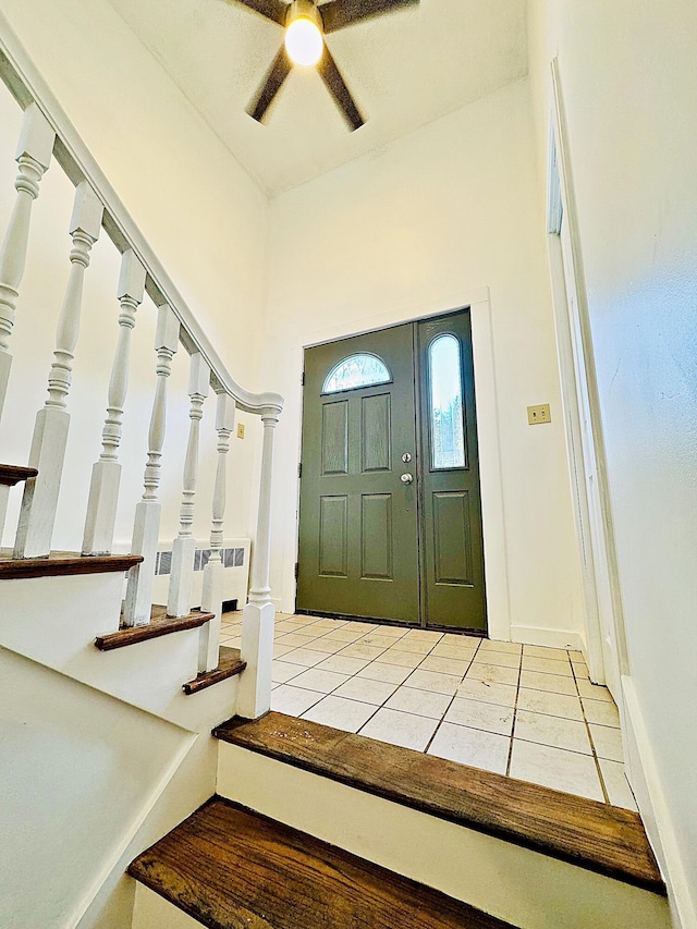 tiled foyer entrance featuring baseboards, stairs, and ceiling fan