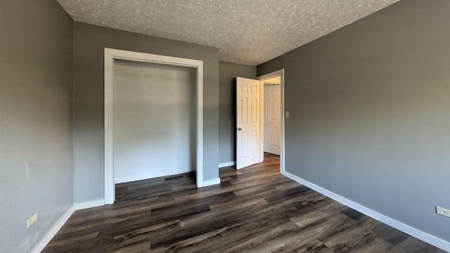 unfurnished bedroom featuring a closet, dark wood finished floors, a textured ceiling, and baseboards