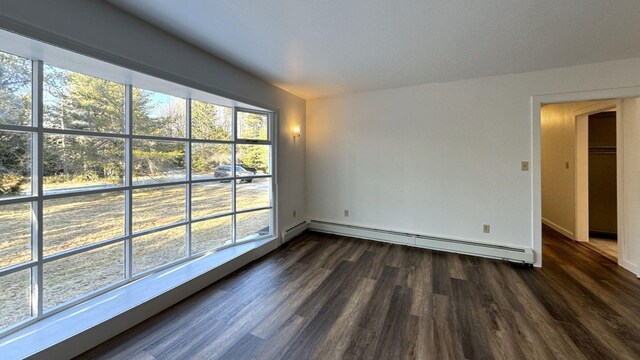 spare room featuring baseboards, baseboard heating, and dark wood-style floors