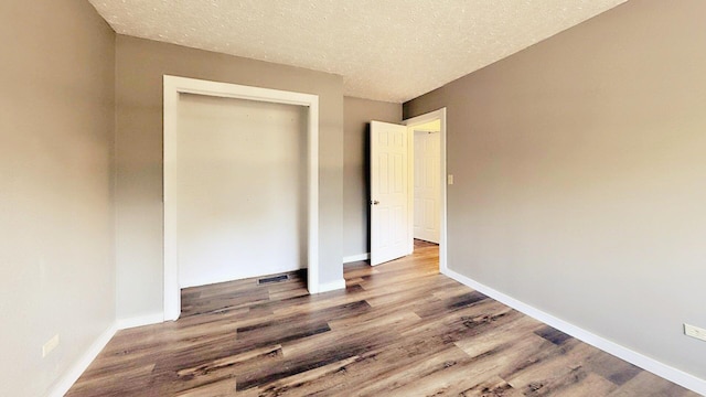 unfurnished bedroom with baseboards, wood finished floors, a textured ceiling, and a closet