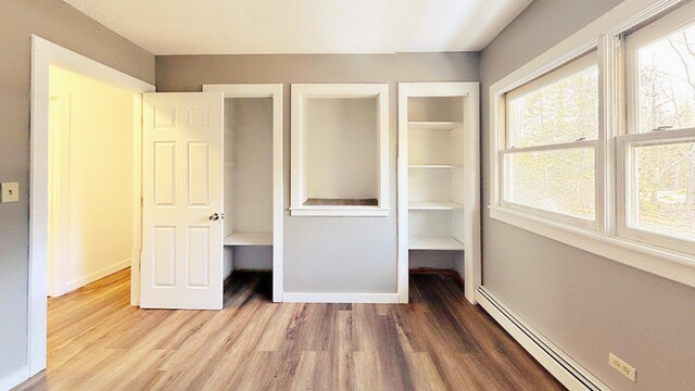 unfurnished bedroom featuring baseboard heating, baseboards, and wood finished floors