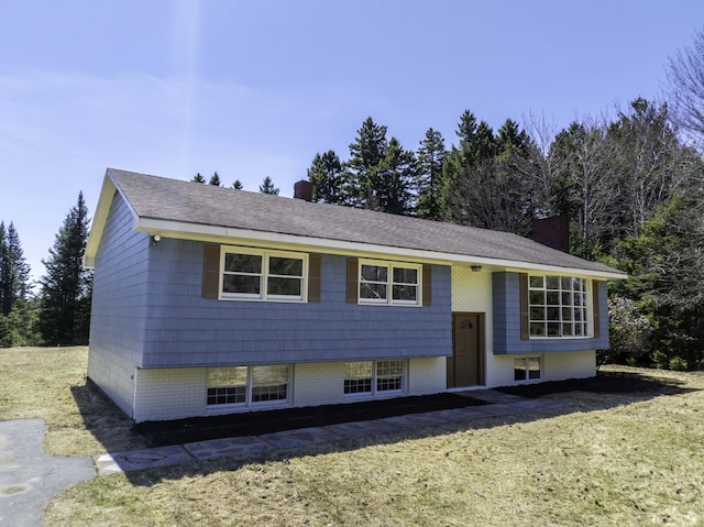 raised ranch featuring a chimney, brick siding, and a front yard