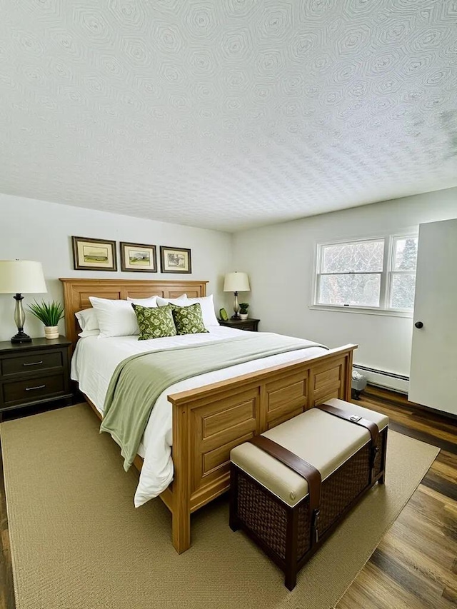 bedroom featuring baseboard heating, wood finished floors, and a textured ceiling