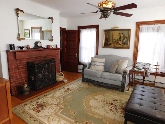 living room featuring ceiling fan, wood-type flooring, and a brick fireplace