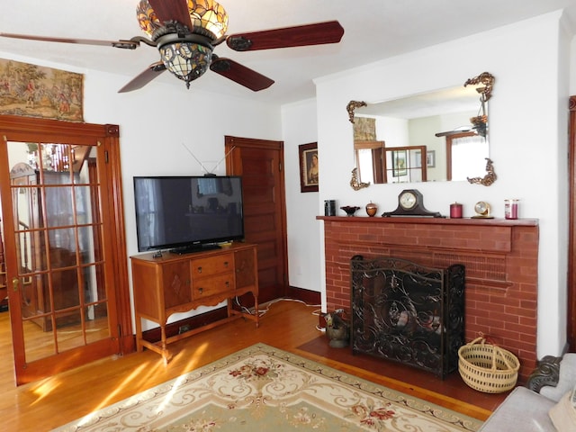 living room with ceiling fan, wood-type flooring, and a brick fireplace