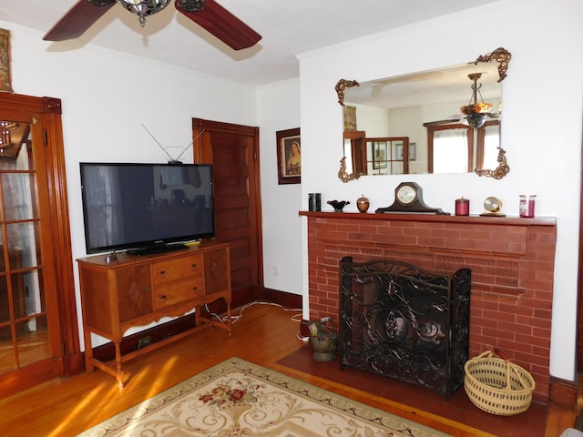 living room featuring hardwood / wood-style flooring, ceiling fan, ornamental molding, and a fireplace