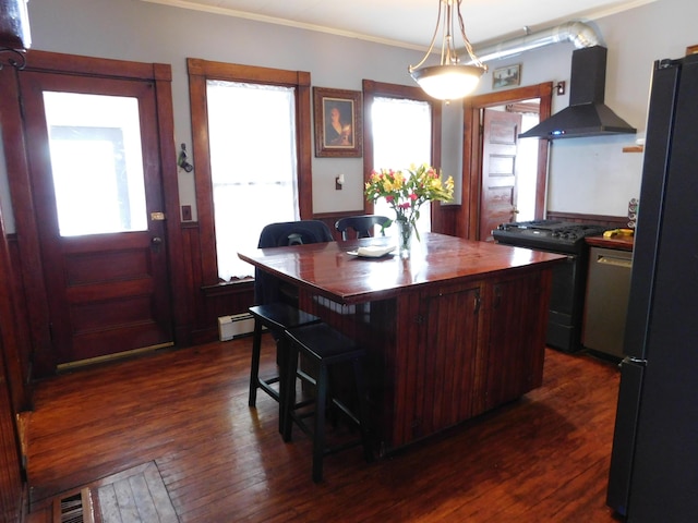 kitchen with range with gas cooktop, black refrigerator, a kitchen breakfast bar, a kitchen island, and wall chimney range hood