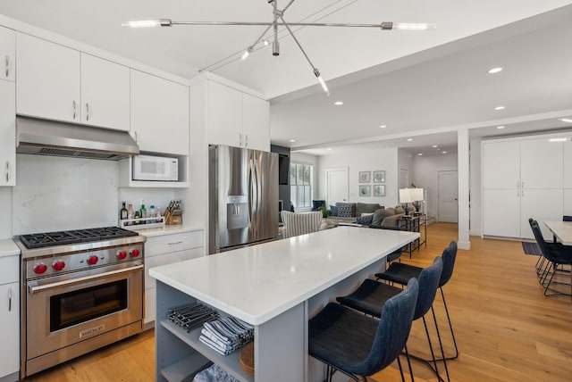 kitchen featuring appliances with stainless steel finishes, a kitchen bar, range hood, and a kitchen island