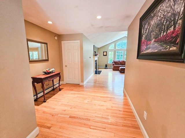 corridor with light wood-type flooring, baseboards, a baseboard heating unit, and lofted ceiling