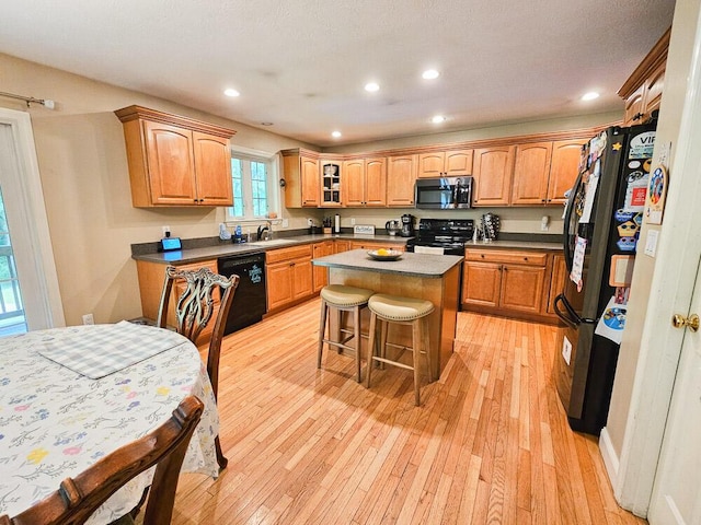 kitchen with dark countertops, a kitchen island, glass insert cabinets, black appliances, and a kitchen bar