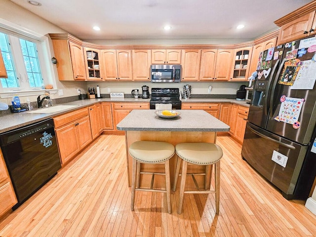 kitchen with a breakfast bar, a sink, a kitchen island, black appliances, and glass insert cabinets