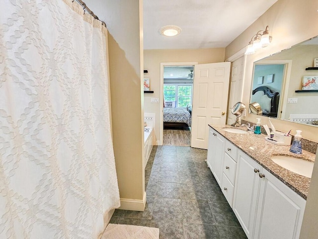 bathroom with double vanity, ensuite bath, baseboards, and a sink