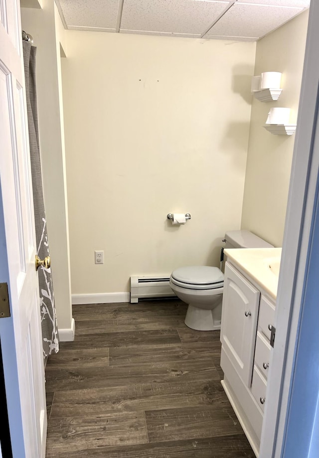 bathroom with a baseboard radiator, hardwood / wood-style flooring, vanity, toilet, and a drop ceiling