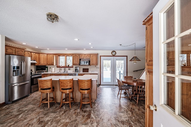 kitchen with a center island, french doors, brown cabinets, stainless steel appliances, and light countertops