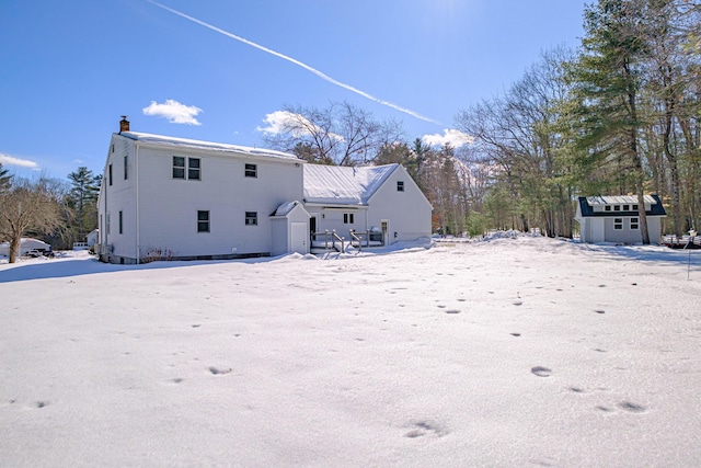 snow covered back of property featuring an outdoor structure, a chimney, and a storage shed