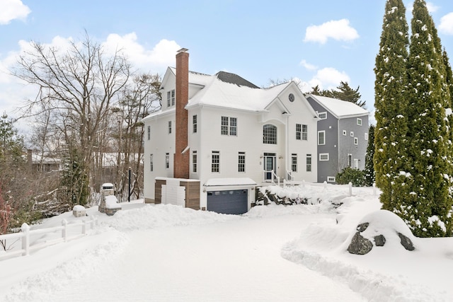 snow covered rear of property with a garage and a chimney