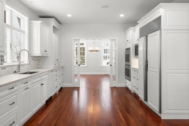 kitchen with light stone counters, a sink, and white cabinets