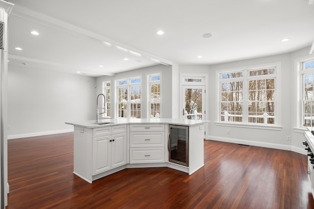 interior space with beverage cooler, a sink, a kitchen island with sink, and white cabinetry