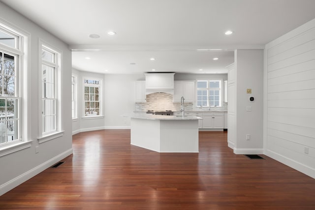 kitchen with an island with sink, dark wood-style floors, white cabinetry, and light stone counters