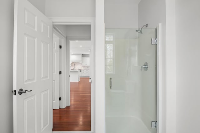 full bath featuring wood finished floors, backsplash, and a shower with shower door