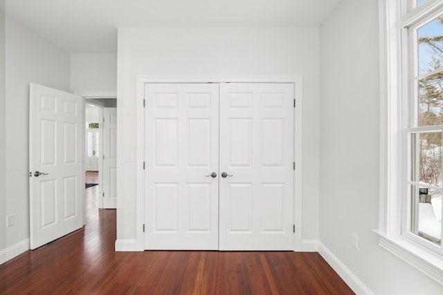 unfurnished bedroom with dark wood-type flooring, a closet, and baseboards