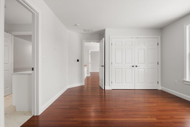 unfurnished bedroom featuring dark wood-style flooring, a closet, and baseboards