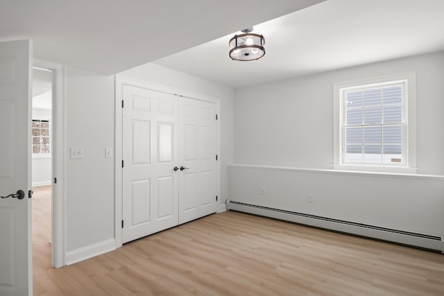 unfurnished bedroom featuring a baseboard radiator, a closet, light wood-style flooring, and baseboards