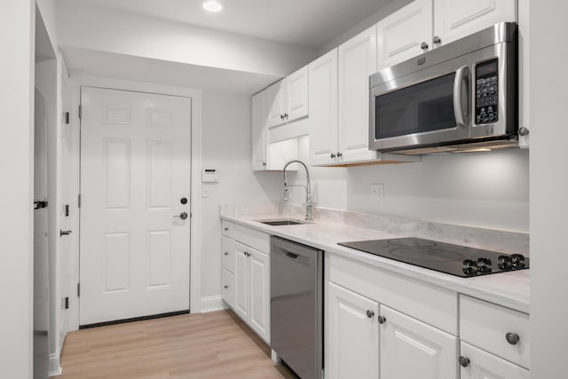 kitchen featuring appliances with stainless steel finishes, light wood-style floors, white cabinetry, and a sink