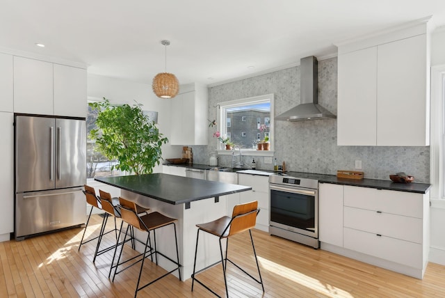 kitchen with dark countertops, appliances with stainless steel finishes, modern cabinets, and wall chimney range hood