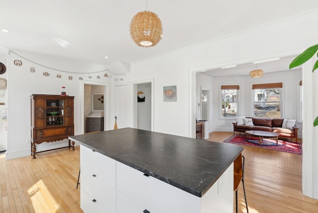 kitchen with a kitchen island, dark countertops, white cabinetry, light wood-style floors, and hanging light fixtures