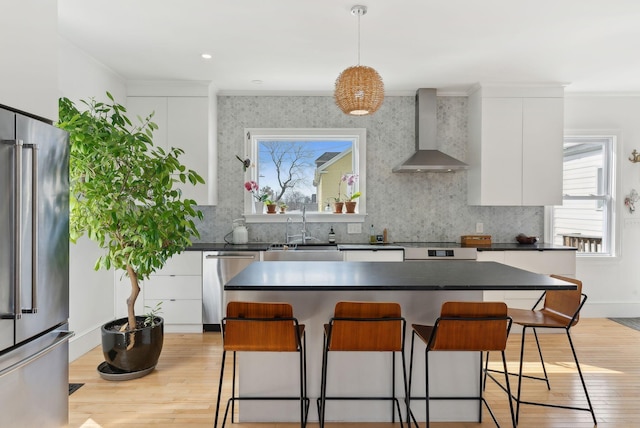 kitchen with stainless steel appliances, a kitchen bar, dark countertops, and wall chimney range hood