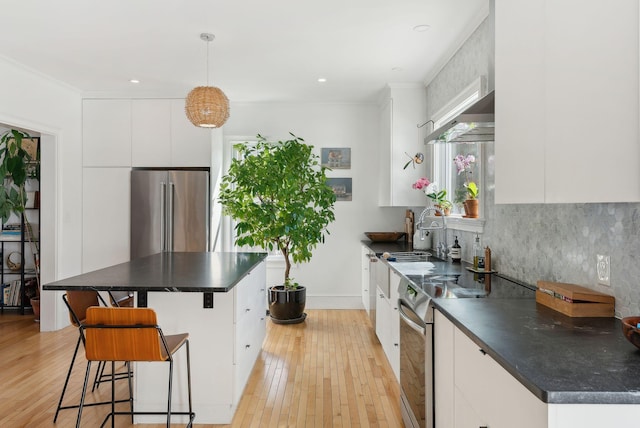 kitchen with dark countertops, light wood finished floors, tasteful backsplash, stainless steel appliances, and a sink