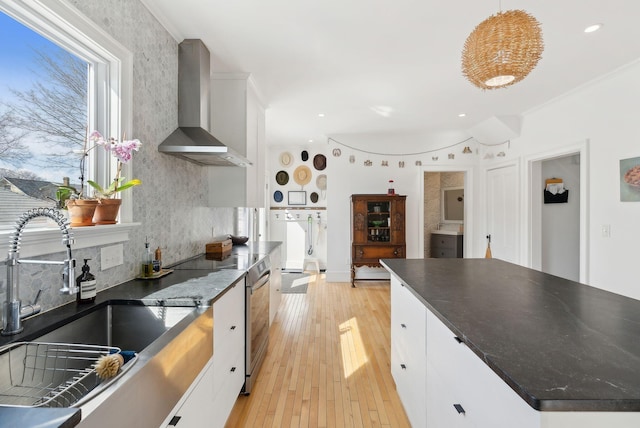 kitchen featuring a sink, stainless steel range with electric stovetop, light wood-style floors, white cabinetry, and wall chimney exhaust hood