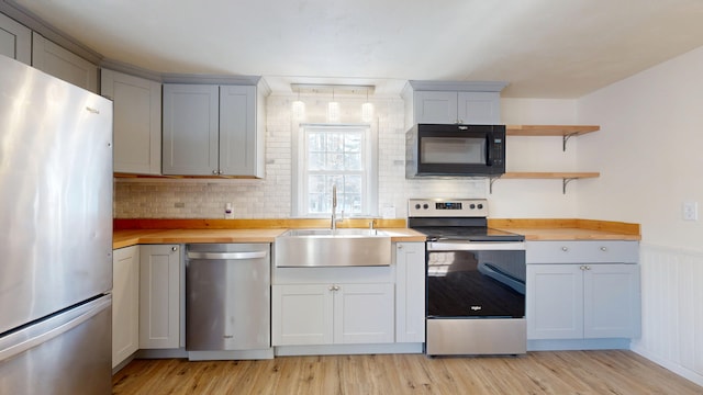 kitchen with appliances with stainless steel finishes, sink, wooden counters, and light hardwood / wood-style floors