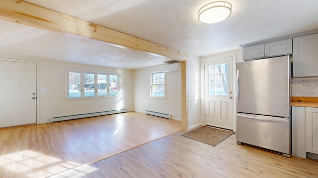 kitchen with baseboard heating, a wall mounted air conditioner, stainless steel fridge, and light hardwood / wood-style flooring