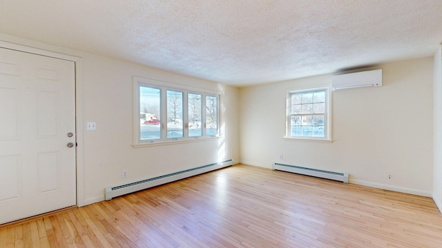 interior space featuring a baseboard heating unit, light hardwood / wood-style flooring, a wall unit AC, and a textured ceiling