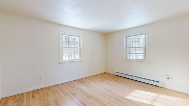 empty room featuring baseboard heating, light hardwood / wood-style floors, and a textured ceiling