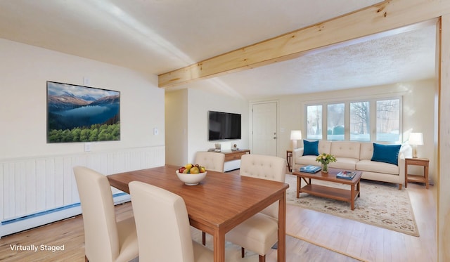 dining area featuring beam ceiling, light hardwood / wood-style floors, and a baseboard heating unit