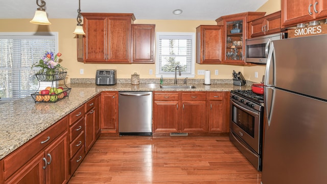 kitchen featuring stainless steel appliances, a sink, light wood-style floors, hanging light fixtures, and glass insert cabinets