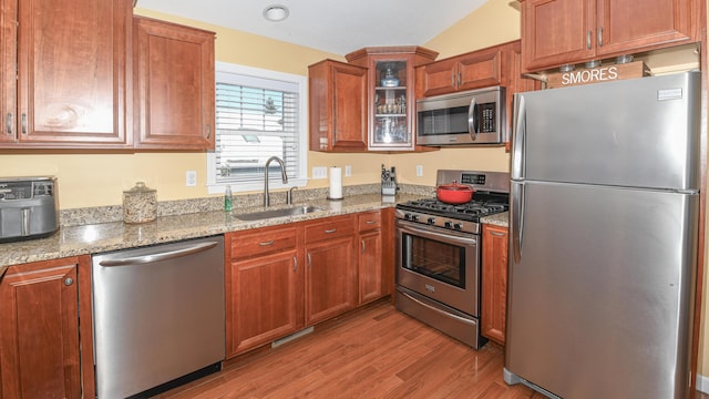 kitchen with a sink, light wood-style floors, appliances with stainless steel finishes, light stone countertops, and glass insert cabinets