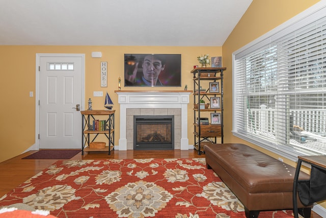 living area with baseboards, a tiled fireplace, and wood finished floors