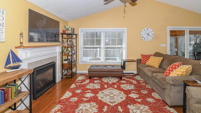 living room with baseboards, a tiled fireplace, ceiling fan, wood finished floors, and vaulted ceiling