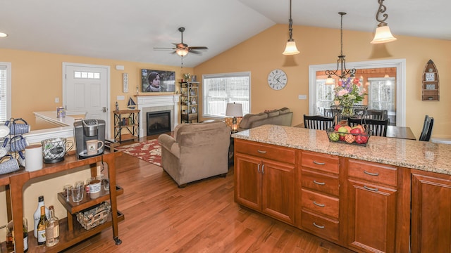 kitchen featuring a tiled fireplace, light wood-style flooring, open floor plan, hanging light fixtures, and light stone countertops