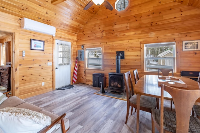 dining room with a wall mounted air conditioner, wooden walls, high vaulted ceiling, a wood stove, and light hardwood / wood-style floors